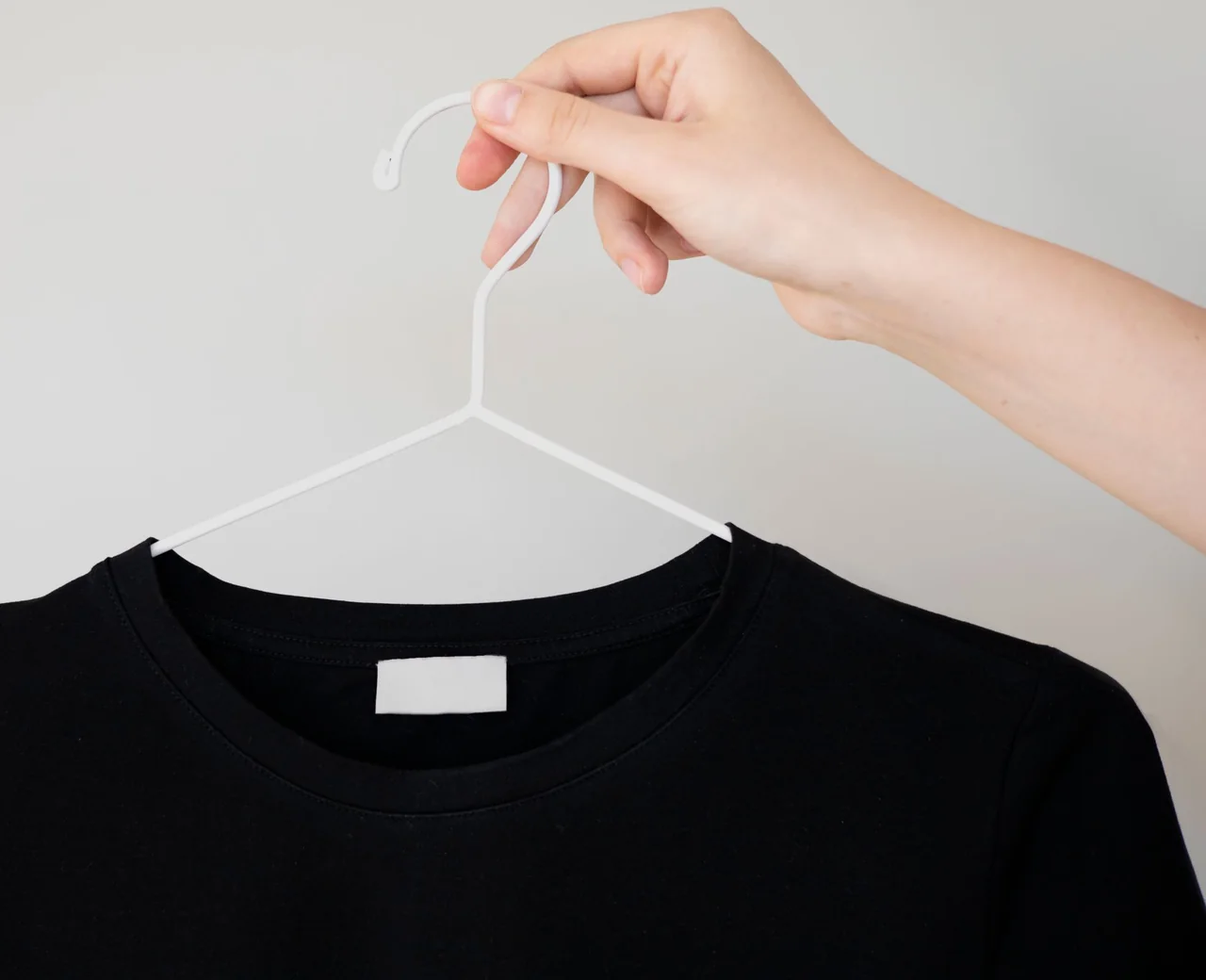 Blank woven neck label sewn into a black crew-neck shirt on a hanger