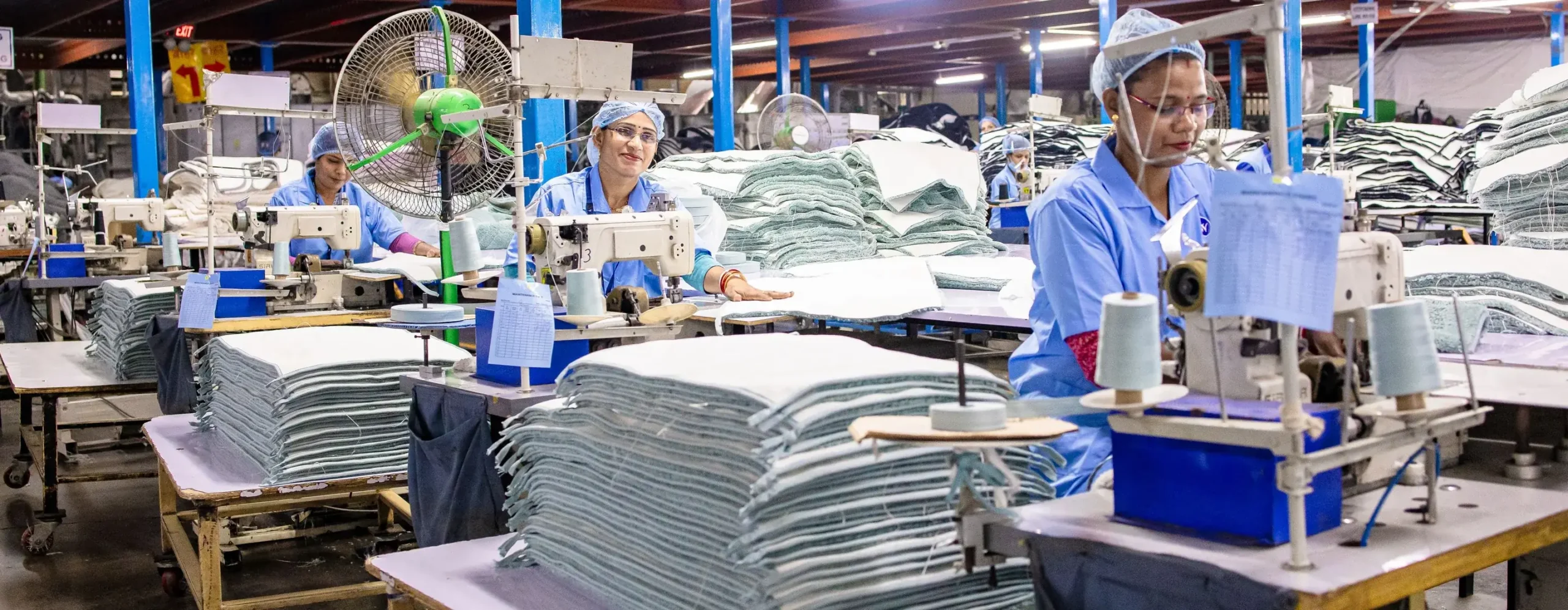 Sewing operators on a sweatsuit production line with stacks of cut fleece panels