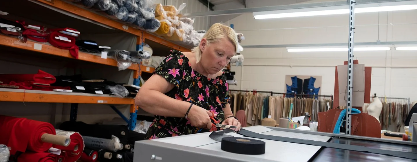 Cutter trimming black fabric at a cutting table with fabric rolls stored behind her