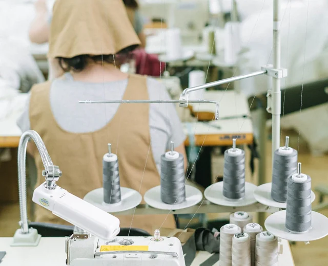 Custom apparel manufacturer production floor with sewing operators and thread spools at their machines
