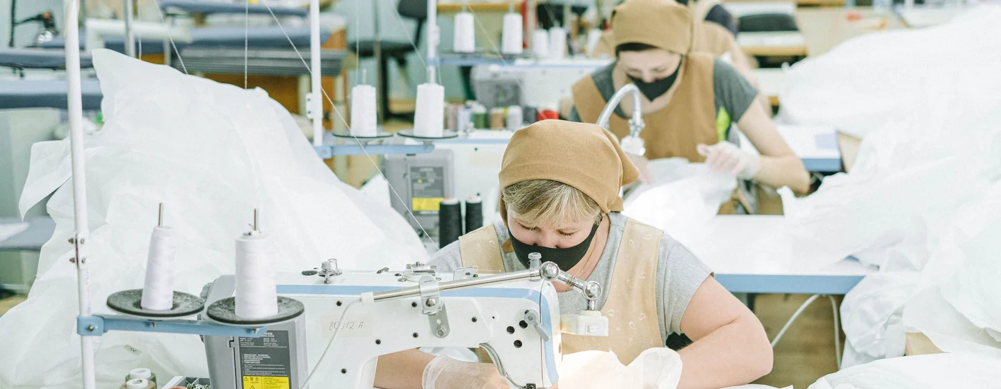 Operators sewing garments at rows of machines in a bright factory workroom