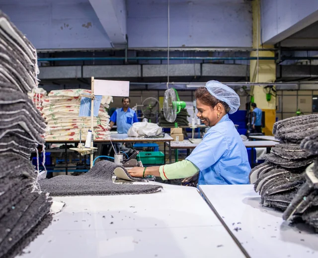 Sewing operator working beside stacks of cut fabric panels on a cut and sew line