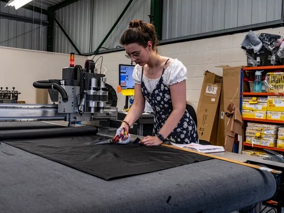 Factory worker cutting dark fabric on an automated cutting table