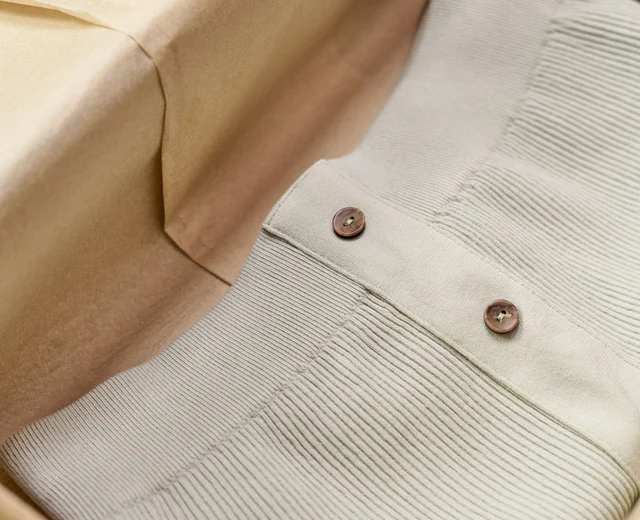 Folded cream knit garment with wooden buttons packed inside a cardboard box