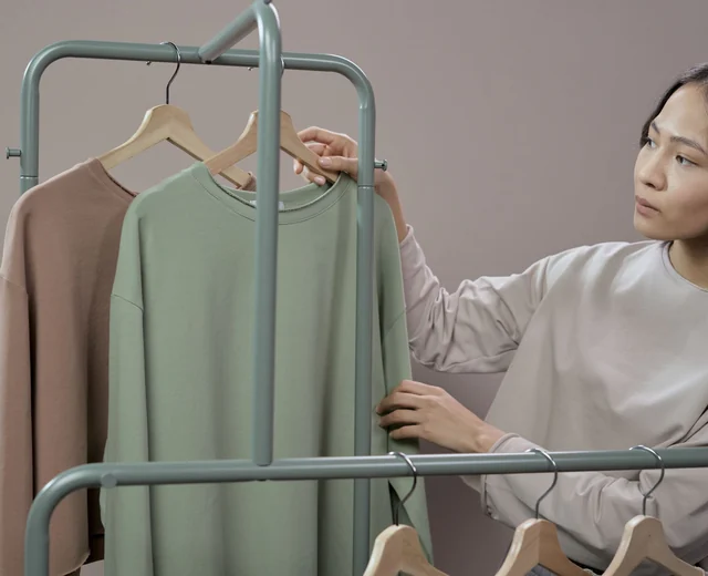 Woman checking a finished sage sweatshirt on a hanger before it is packed