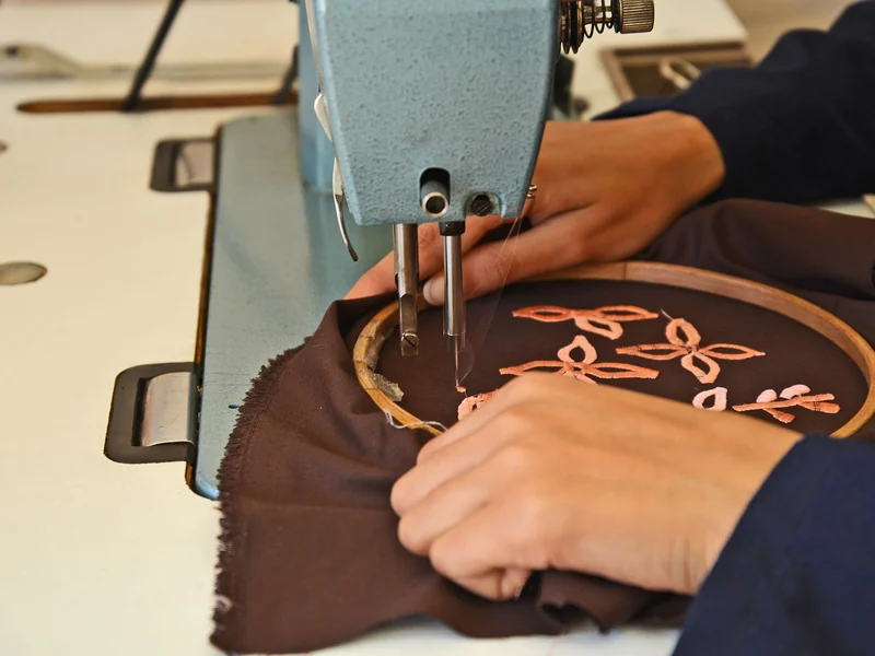 Operator embroidering a logo design on dark jacket fabric in a hoop