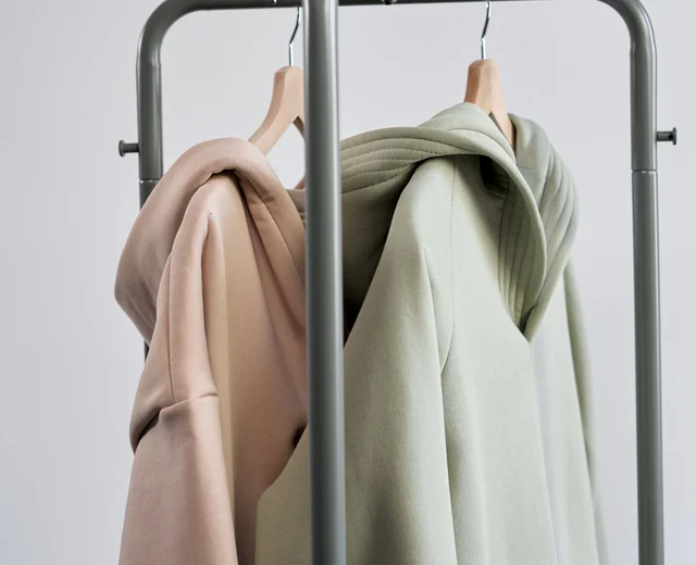 Pink and sage hoodies on hangers, finished garments from a private label apparel manufacturer