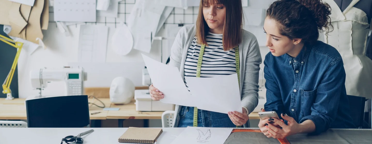 Two production staff reviewing a garment spec sheet at a studio worktable