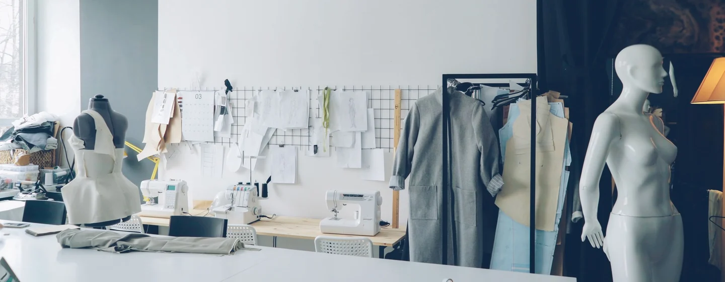 Sample room with dress forms, pattern sheets on the wall and sewing machines