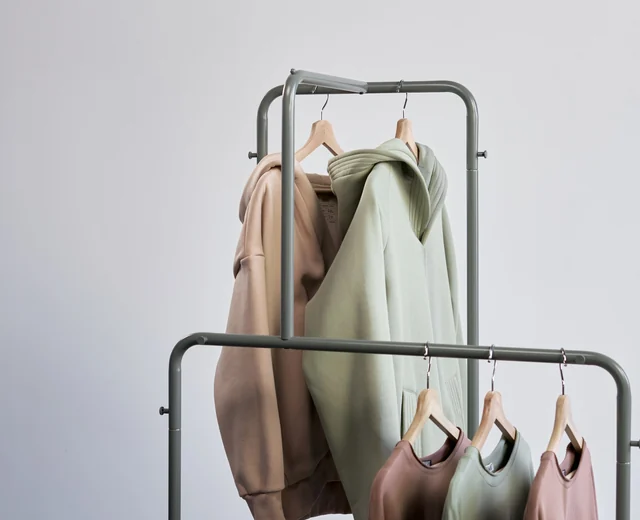 Hoodies and sweatshirts in sage, sand and mauve hanging on a small clothing rail