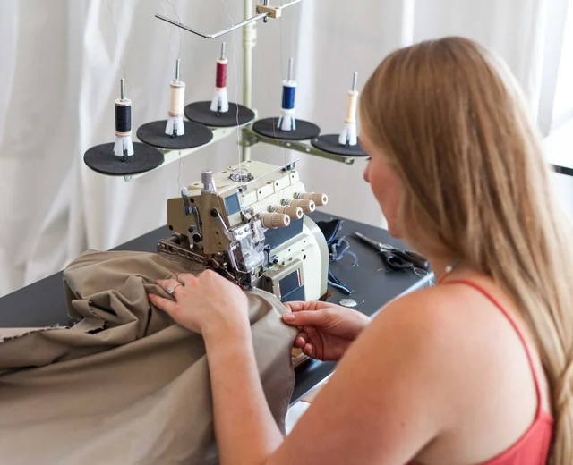 Seamstress sewing a sand-colored fabric panel on an overlock machine